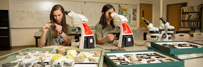 2 students looking through microscopes in a Geology lab