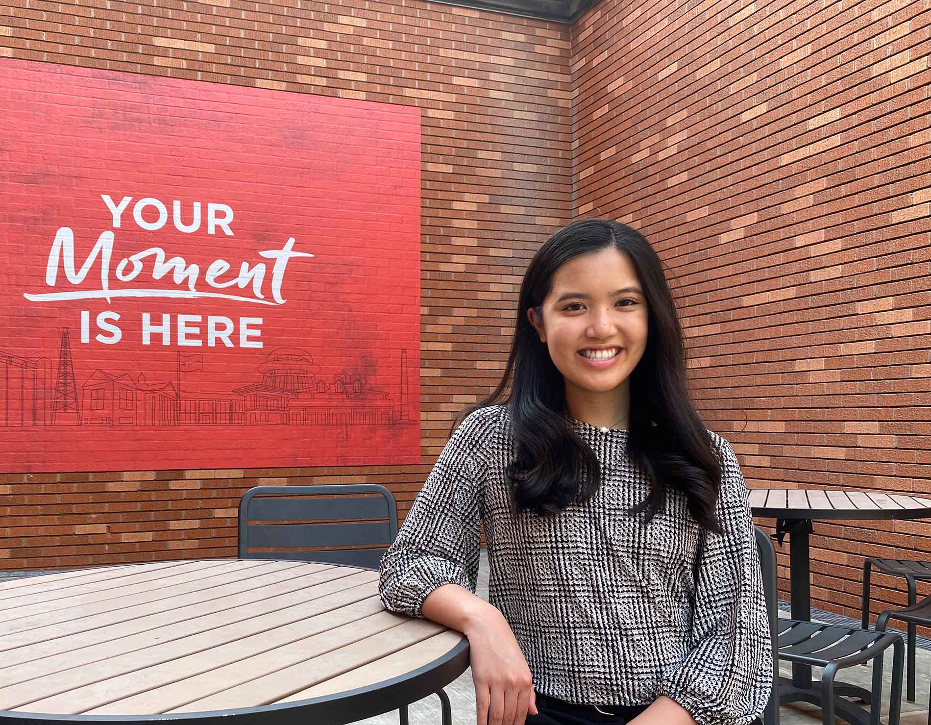 Tiffany Tran sitting in front of "Your Moment is Here" mural on campus
