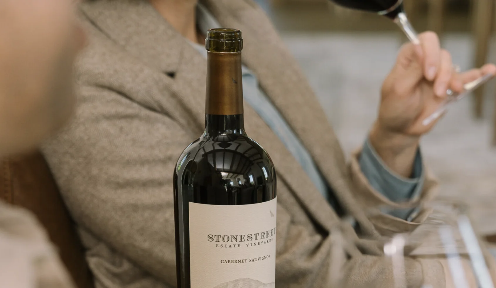 About Stonestreet Estate Vineyards- Picture of a wine bottle, someone in the background drinking a glass of wine