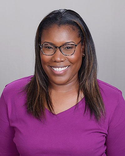 Dionne Babineaux, image of smiling african american woman with long hair and glasses in purple shirt