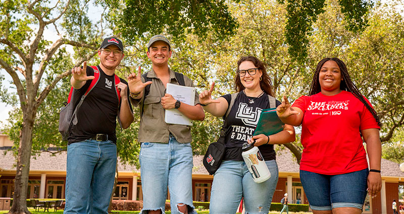 Four students facing the camera making L shape with fingers