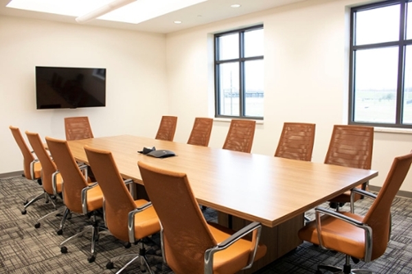 Small, bright room with several orange chairs surrounding a wooden table with medium-sized windows, and a television on one wall.