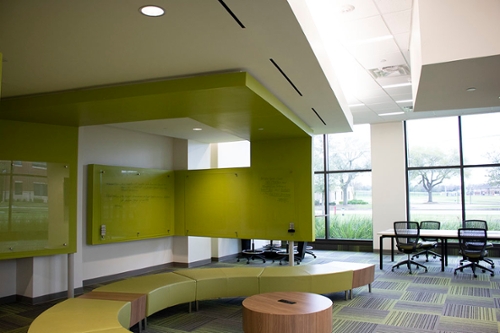 Medium sized room with large-paned windows, green walls framing a glass marker board with a curving bench and a wooden table lined with chairs.