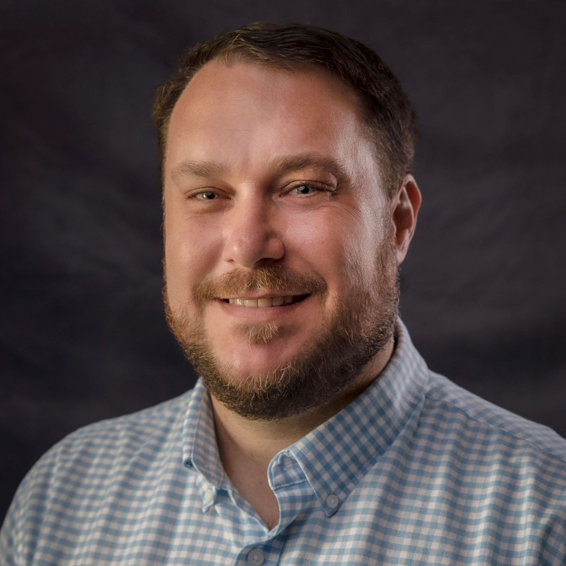 james scales, headshot of smiling man with beard in blue and white checked shirt