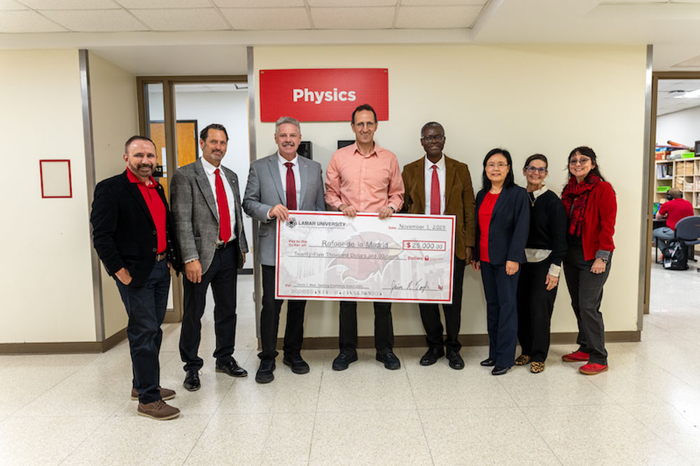 2025 David J. Beck Teaching Excellence award recipient rafael de la madrid, 8 men and women standing in front of Physics sign with man holding oversize check