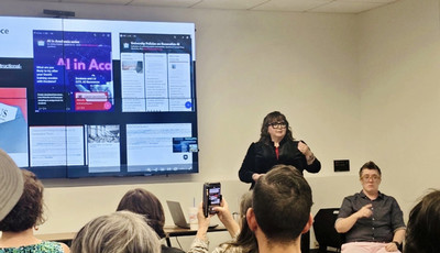 Welcome Week, woman in black speaking before a class, presentation on screen behind her