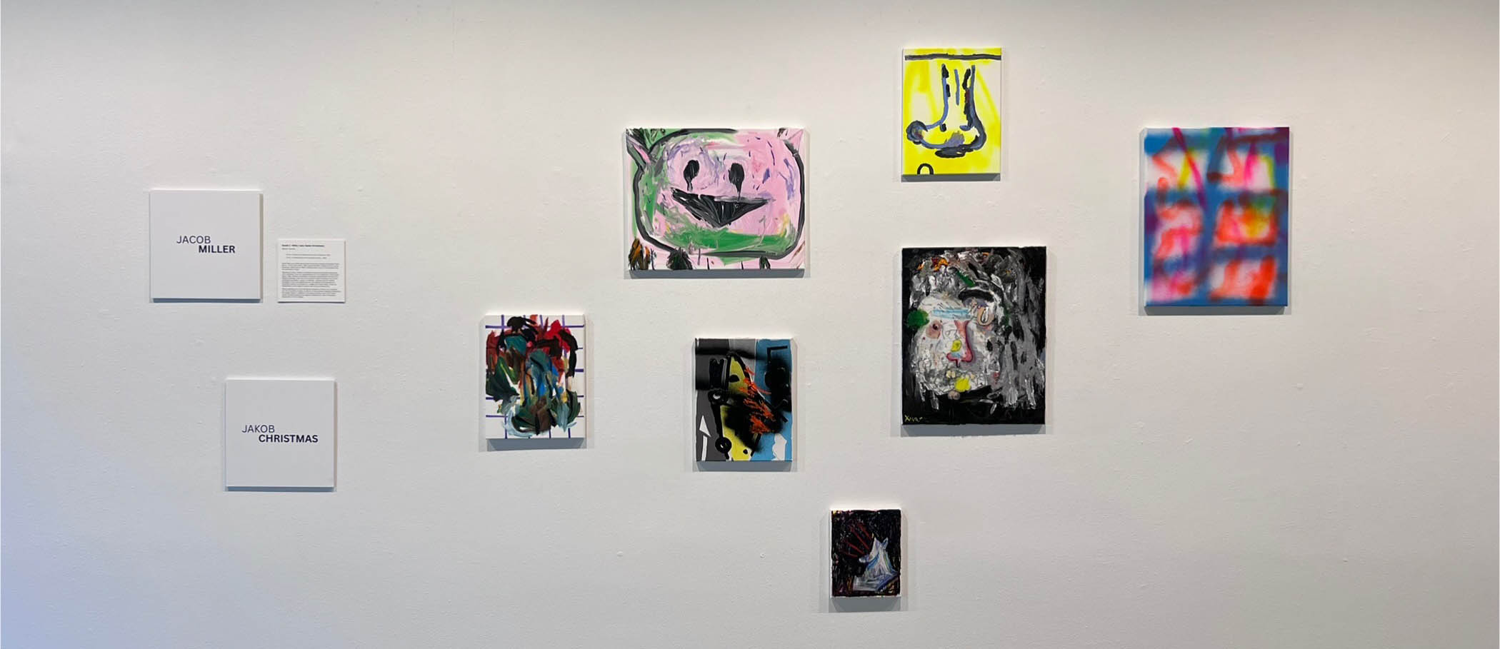 Abstract art exhibit with various colorful paintings on a white wall.