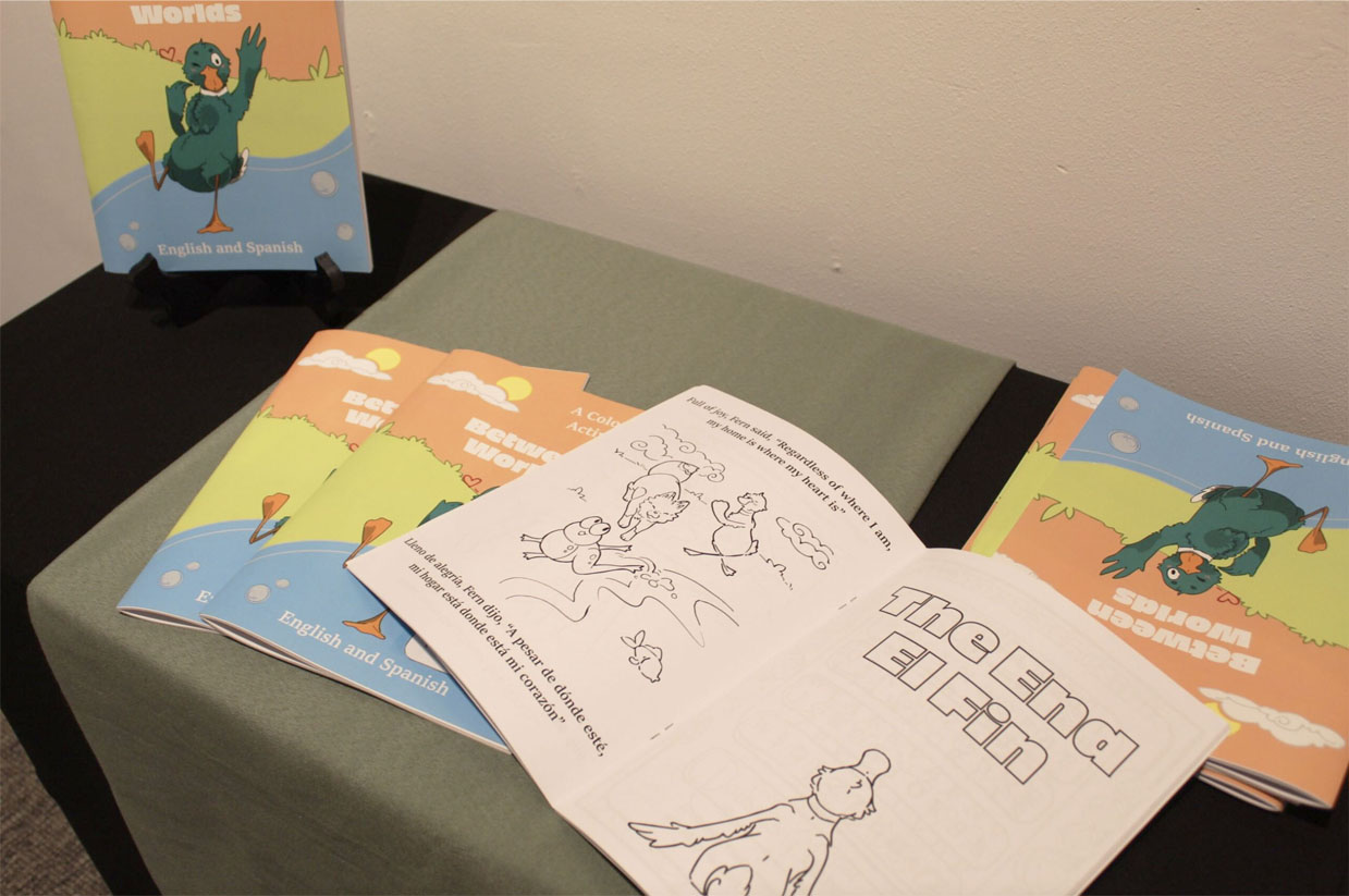 Display of children's activity books titled "Between Worlds" on a table, with one book open showing coloring pages.