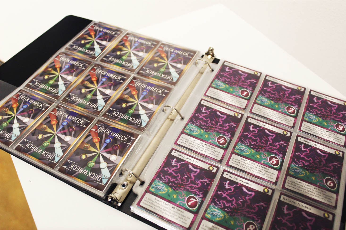 An open binder displaying trading cards titled "Deck Wreck" and "Raging Nimbus."