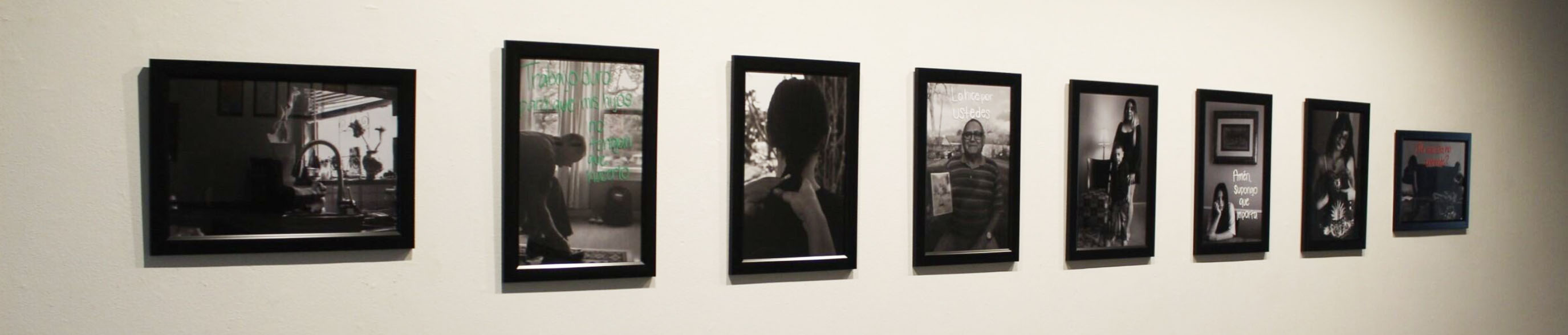 A row of eight framed black and white photographs on a gallery wall.