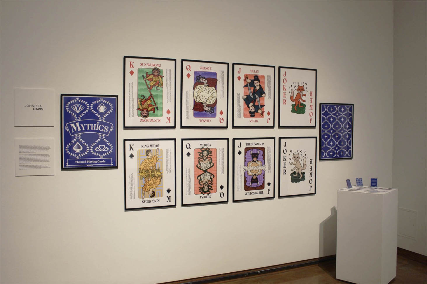 An art exhibit featuring large playing cards with mythological figures displayed on a gallery wall.