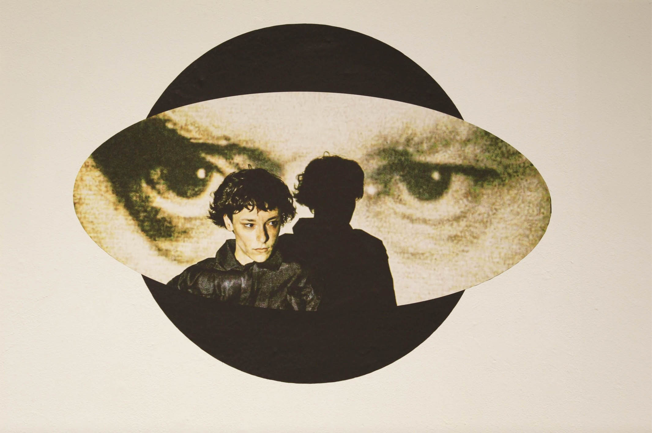 A person stands before a large image of intense eyes, surrounded by a black circular frame.