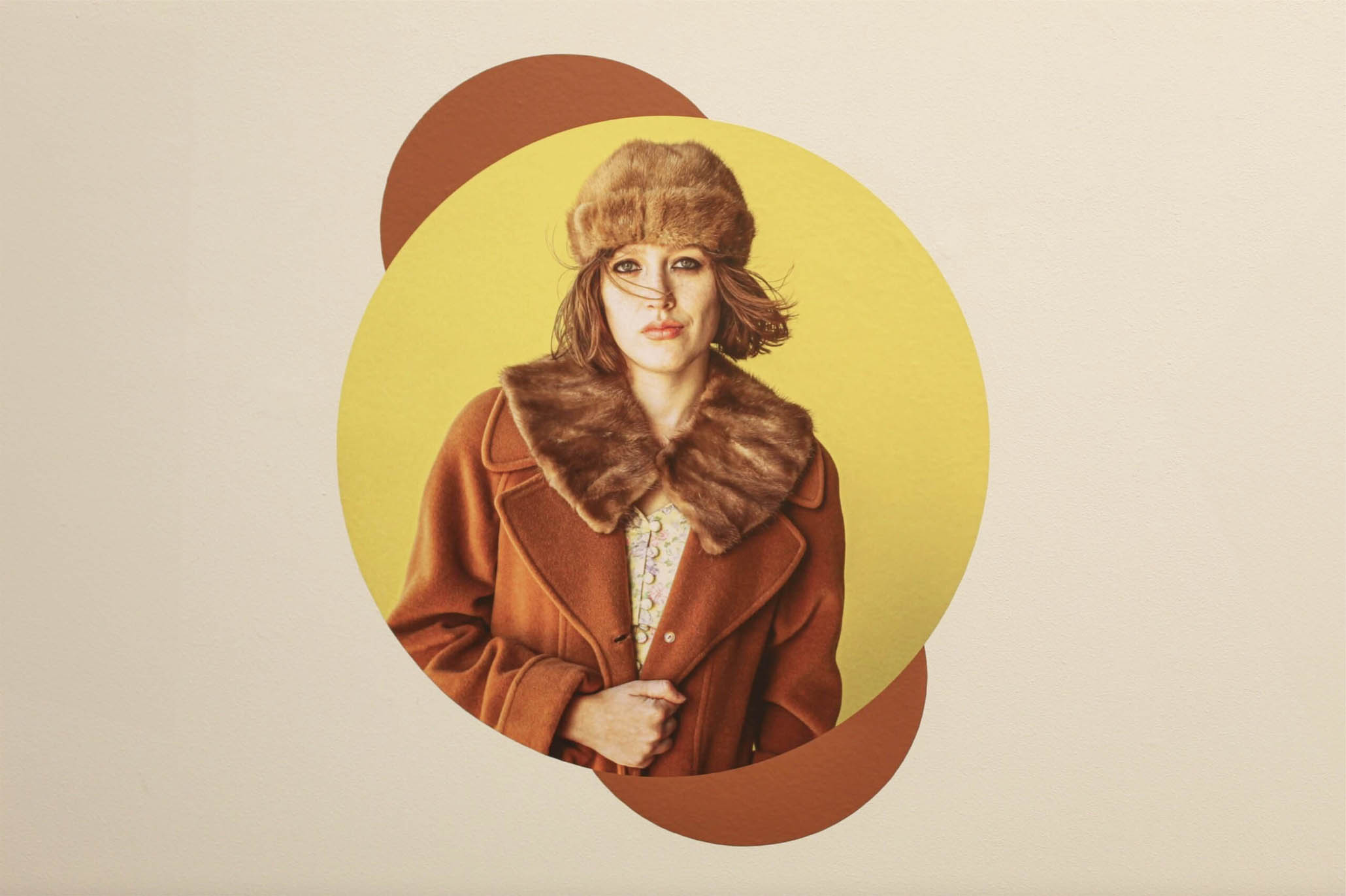 Person in a brown fur-collared coat and hat against a yellow and brown circular background.