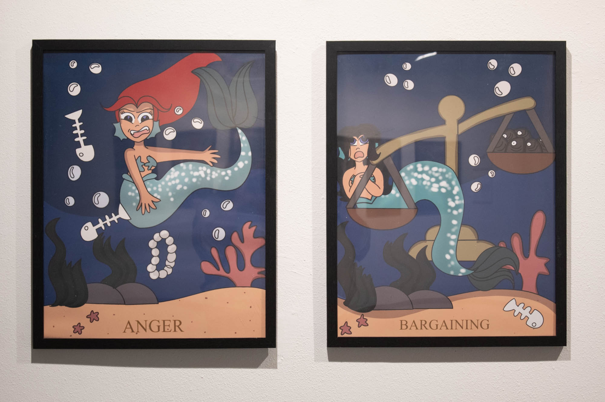 Two framed illustrations of cartoon mermaids, one labeled "ANGER" and the other "BARGAINING," showcasing exaggerated expressions under the sea.
