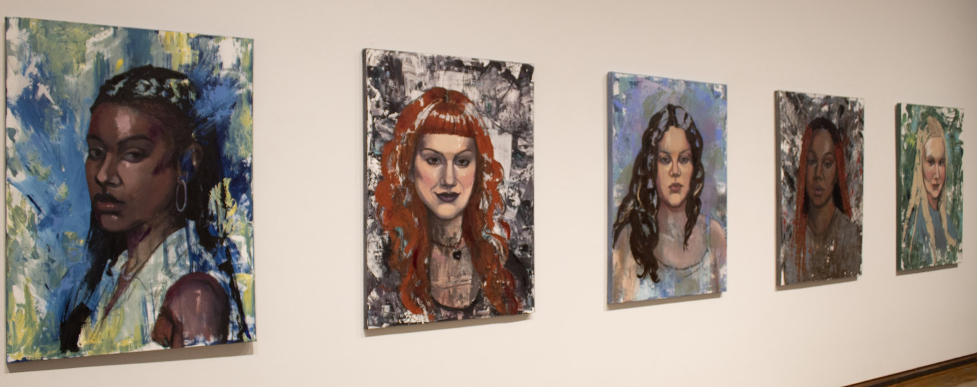 A series of five painted portraits of women on a gallery wall, each with unique backgrounds and styles.