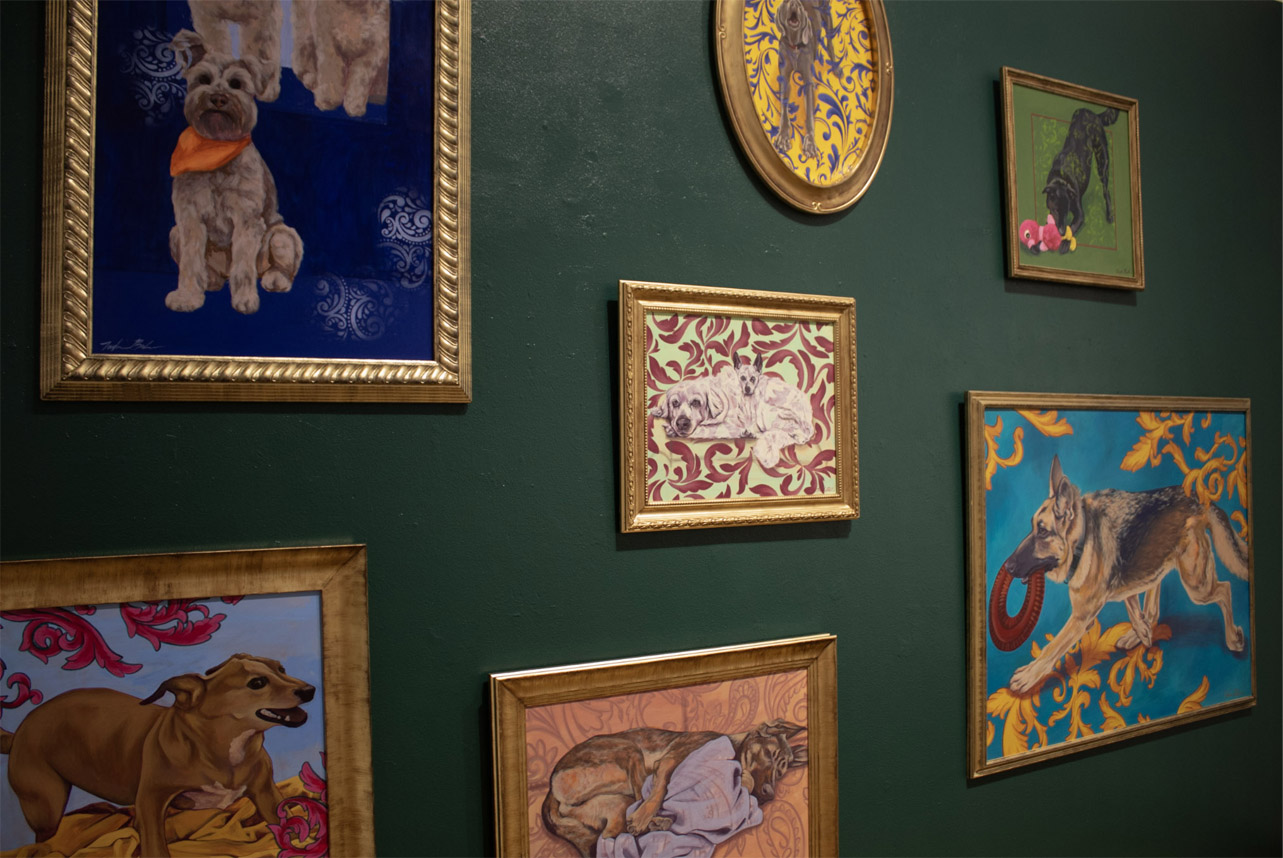A collection of framed dog paintings on a green wall, featuring various dogs in colorful, patterned backgrounds.