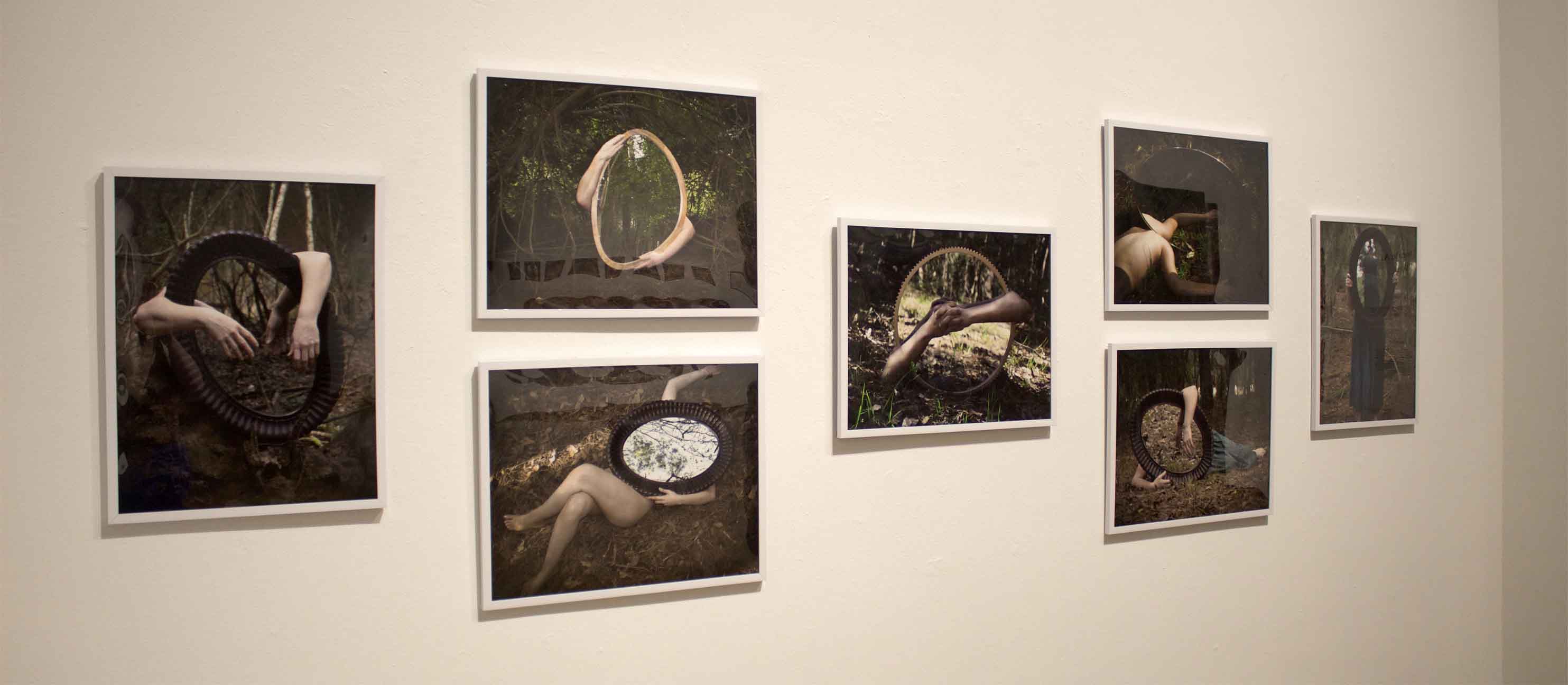 Art installation of seven framed photographs featuring surreal scenes with mirrors and human limbs outdoors.