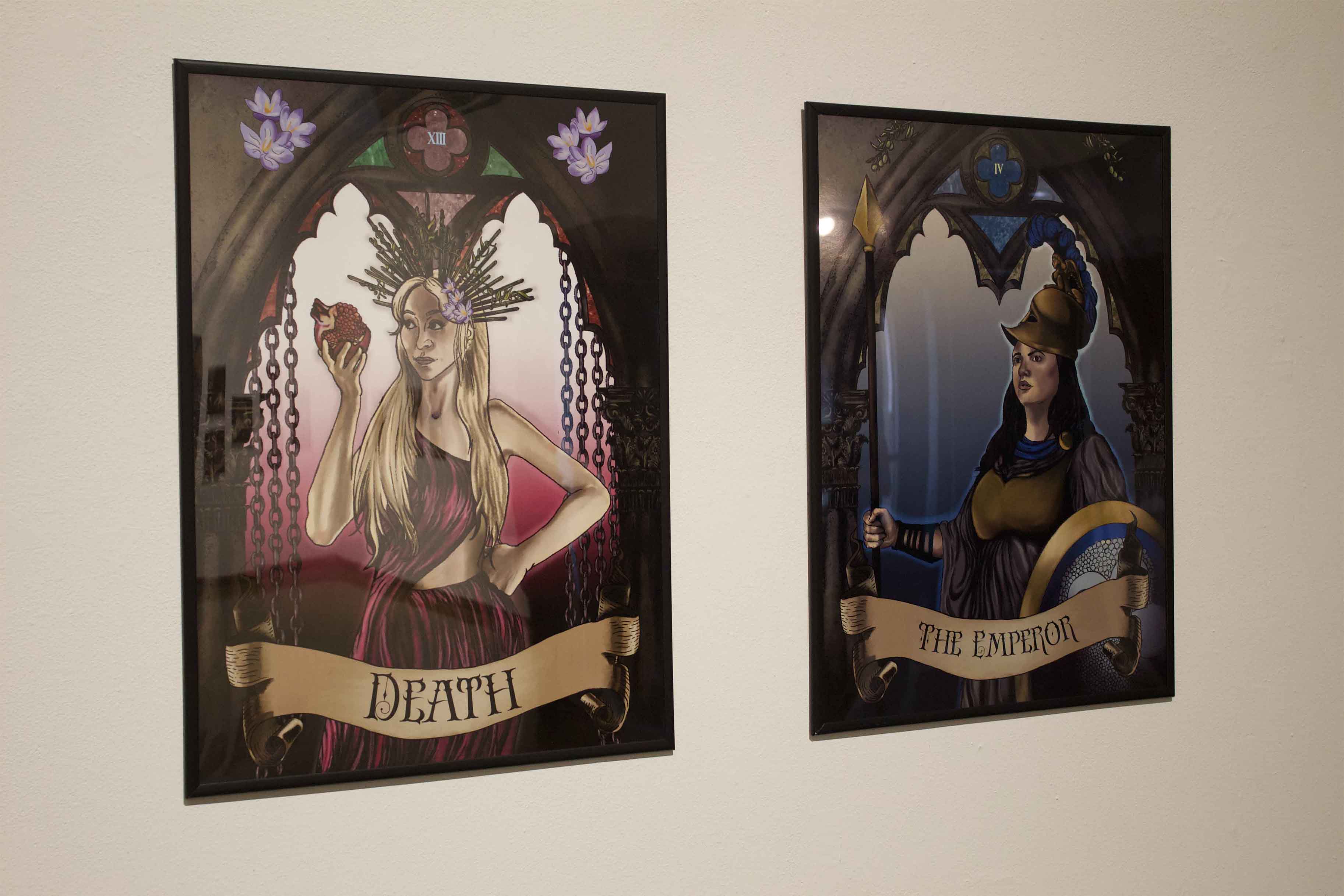 Two framed tarot-themed artworks on a wall, titled "Death" with a blonde woman and "The Emperor" with a dark-haired woman.