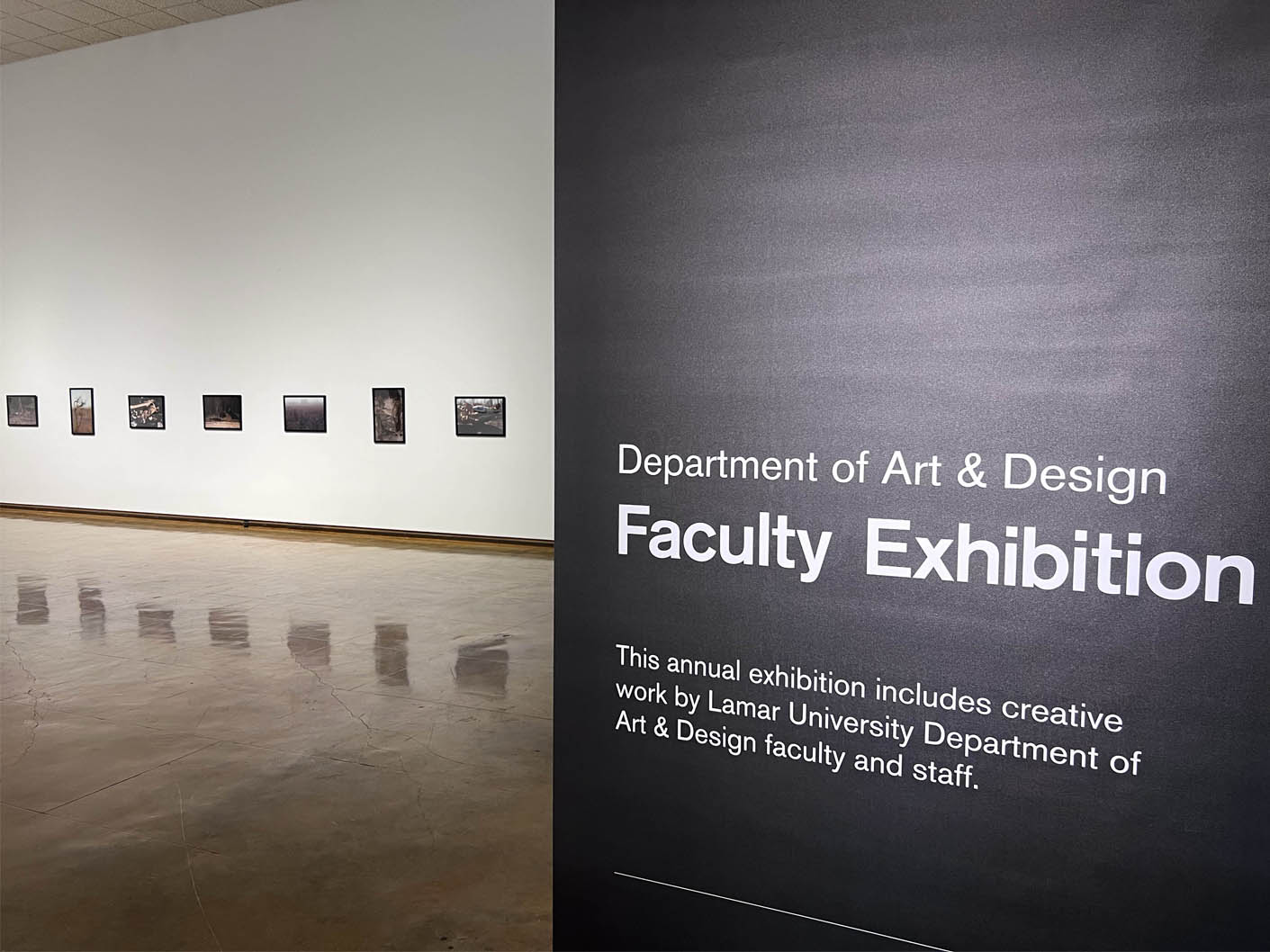 Art exhibition with a large display banner and framed artworks on a white wall.