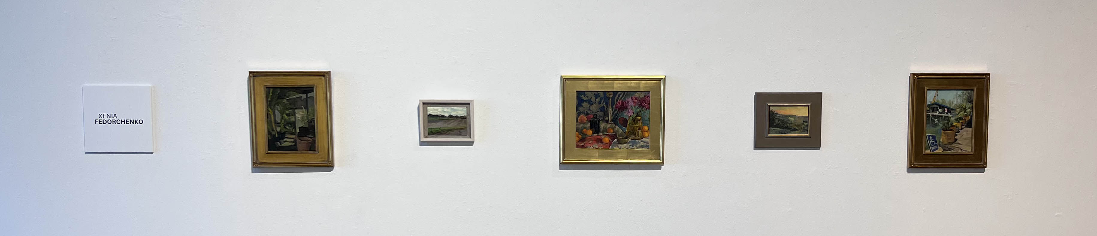 A gallery wall displaying five framed paintings and a name plaque for Xenia Fedorchenko.