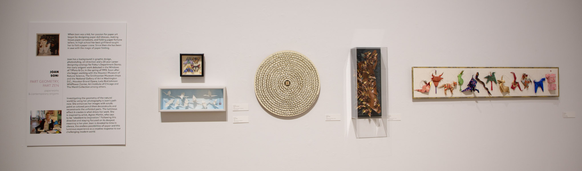 Art gallery wall with artworks by Joan Son, including origami and geometric designs.