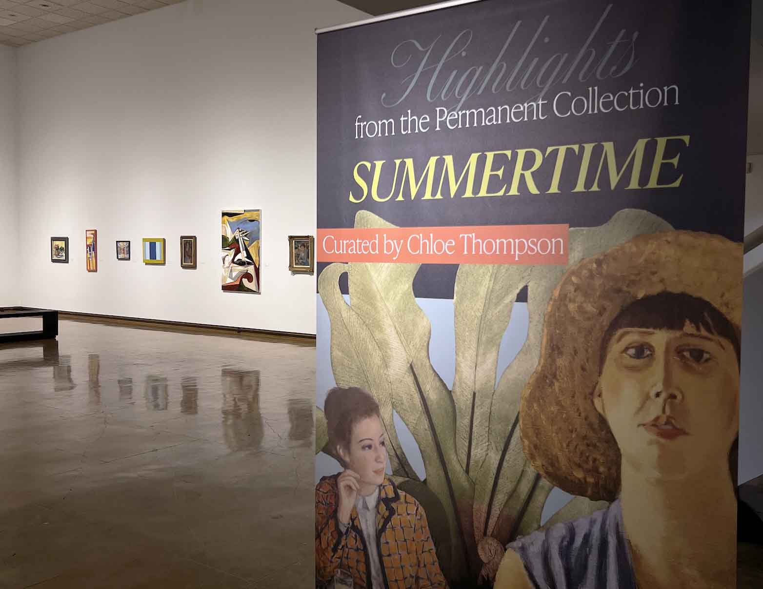 Art gallery with a display of framed artworks and a vertical sign with text and artwork.