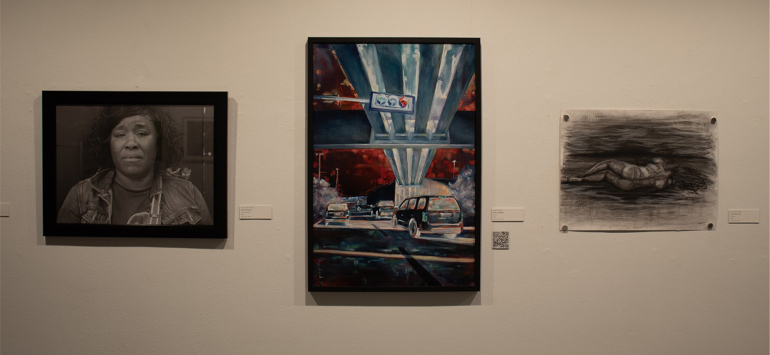 A gallery wall displays three artworks: a black-and-white portrait of a woman, a colorful painting of cars under an overpass, and a charcoal drawing of a reclining figure.