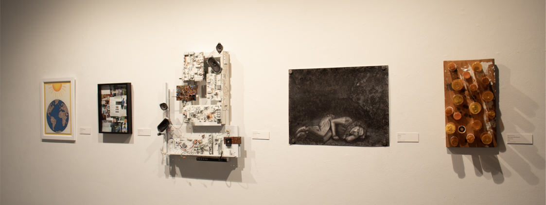 A gallery wall featuring four artworks: a colorful globe illustration, a collage of photographs, a mixed media installation with electronic components, and a monochromatic drawing of a curled figure in a dark background.