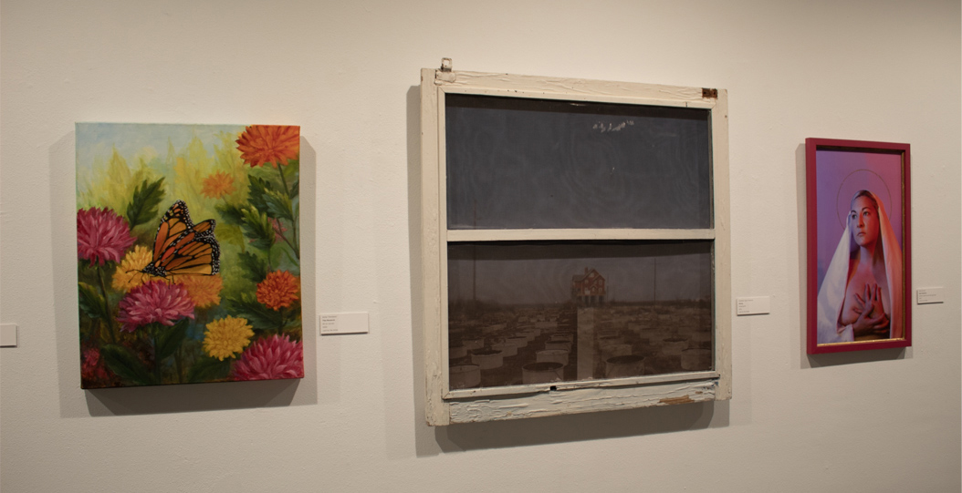 A gallery wall features three artworks: a colorful floral painting with a butterfly on the left, a sepia-toned photograph in a weathered window frame in the center, and a portrait of a young woman in a veil on the right.