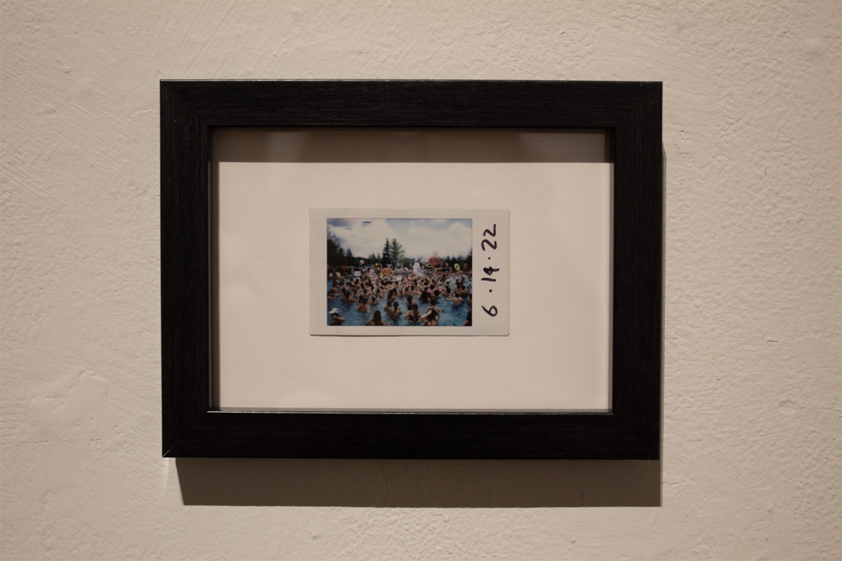 A framed polaroid photo of a crowded swimming pool on a sunny day, with the date "6.14.22" handwritten on it.