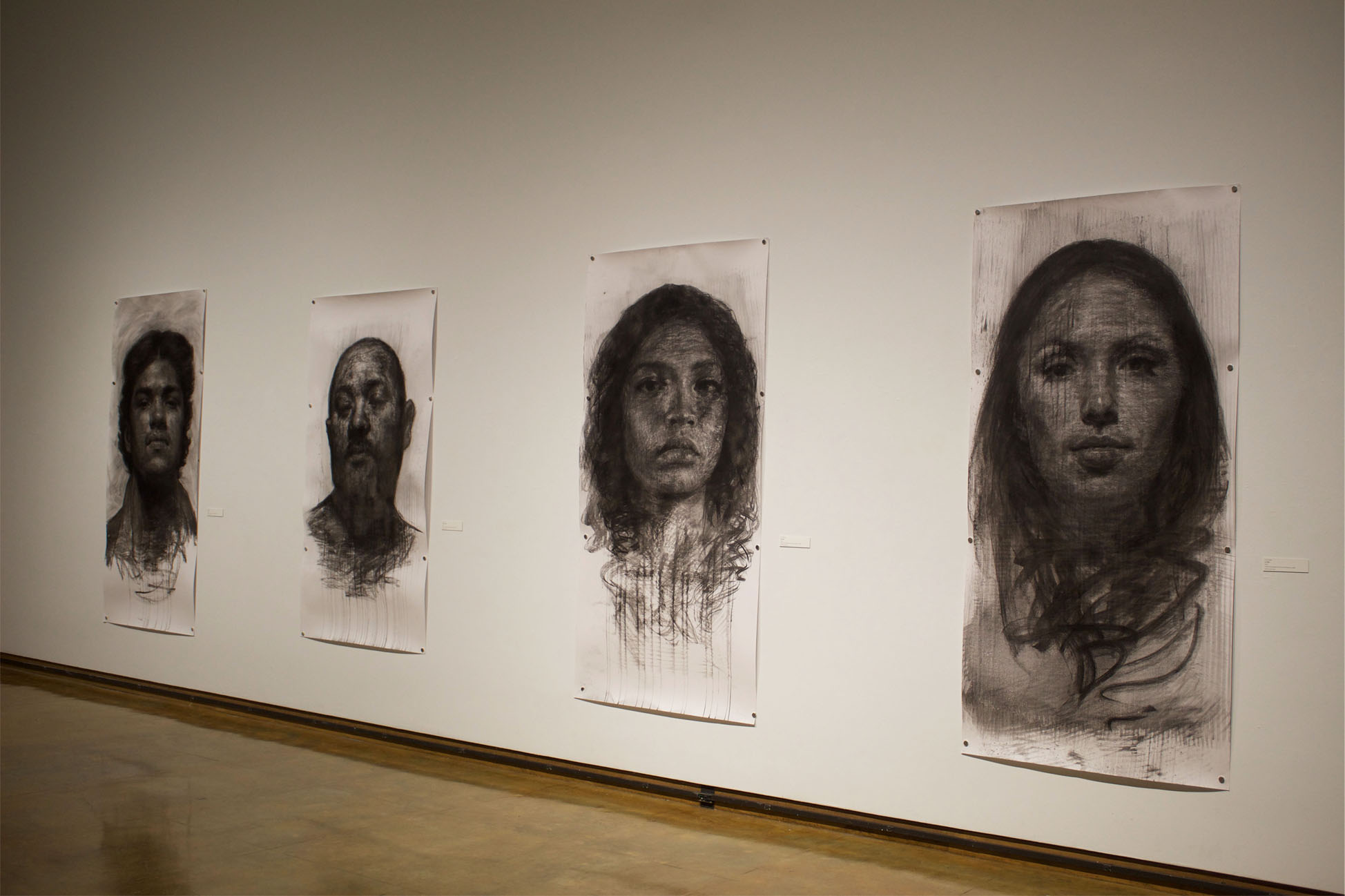 Charcoal portraits of four faces displayed on a gallery wall.