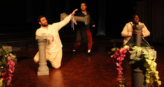 three men singing next to pedestals draped with foliage