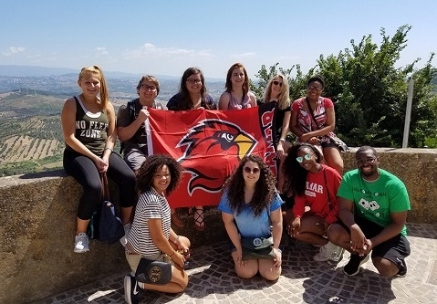 Psychology in Italy, students sitting on ledge holding flag with LU Cardinal logo
