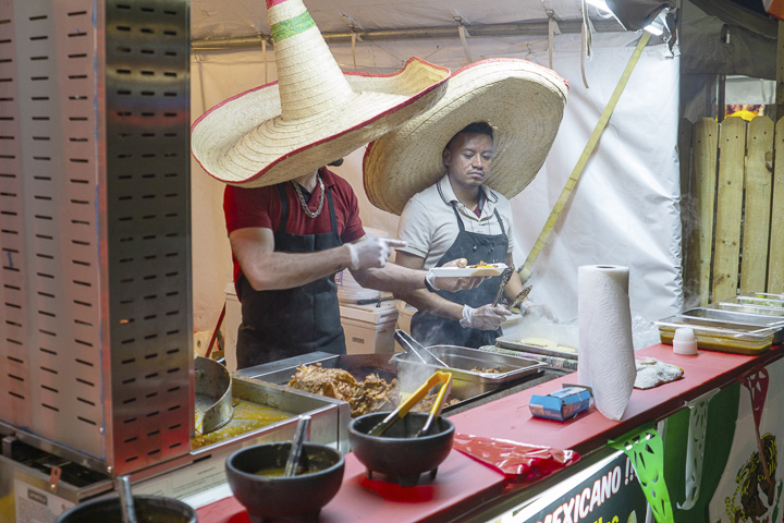 Food vendors from “La Salsita” food booth, middle left, prepare a taco plate for customers while sporting large sombreros. UP photo by Lakota Jaton