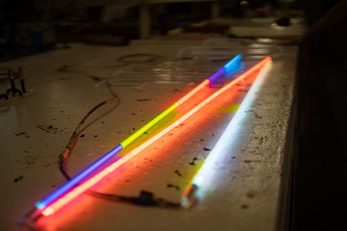 Dobelmann lights up three pieces of glass tubing, one with different colored glass, another with a clear piece of glass with a color powder filled with neon, and a final tube with glass and powdered color to filled with argon to show how the different gasses affect the colors.